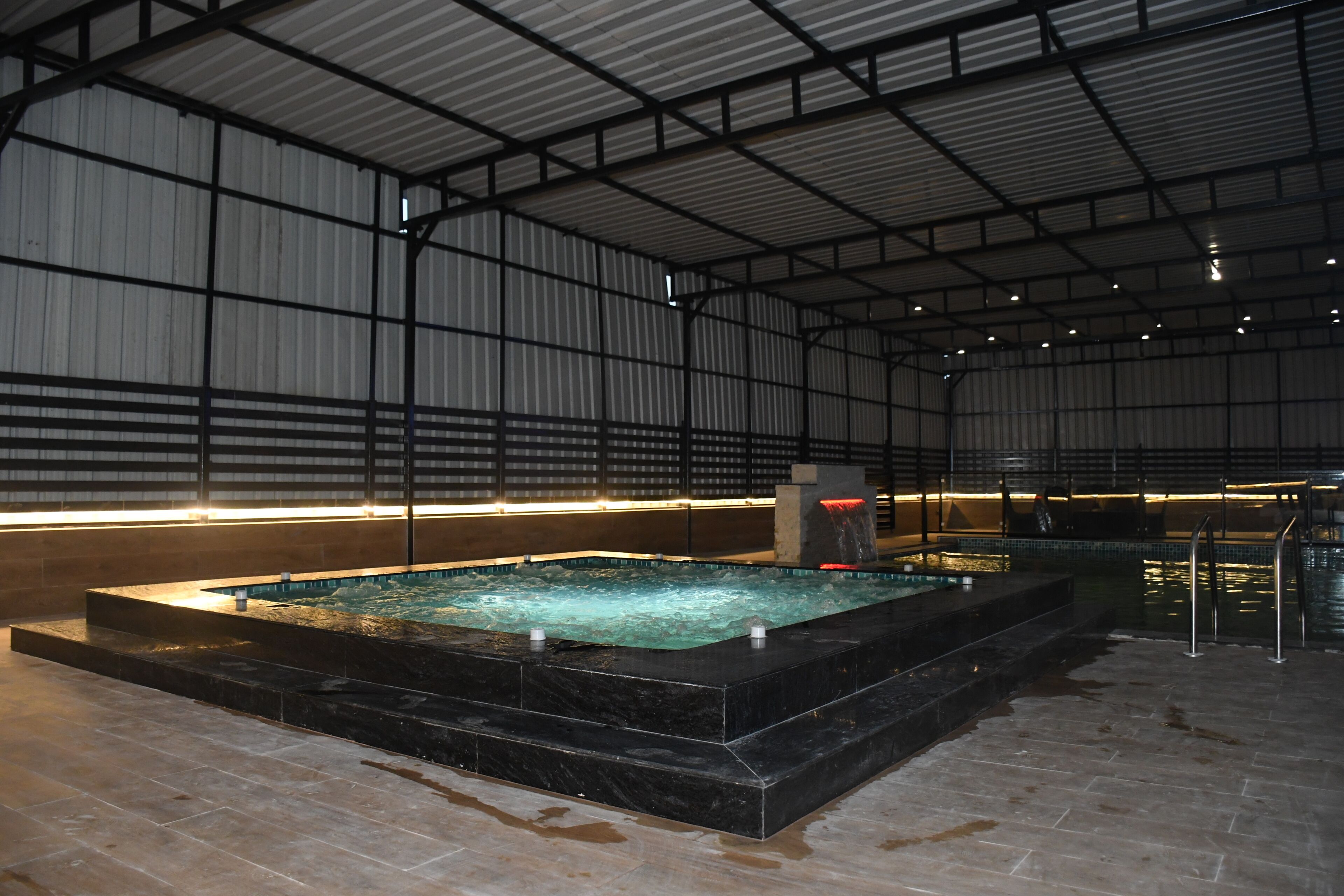Una piscina interior con suelo de baldosas, rodeada por paredes metálicas y un techo alto.