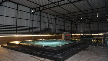 Una piscina interior con suelo de baldosas, rodeada por paredes metálicas y un techo alto.