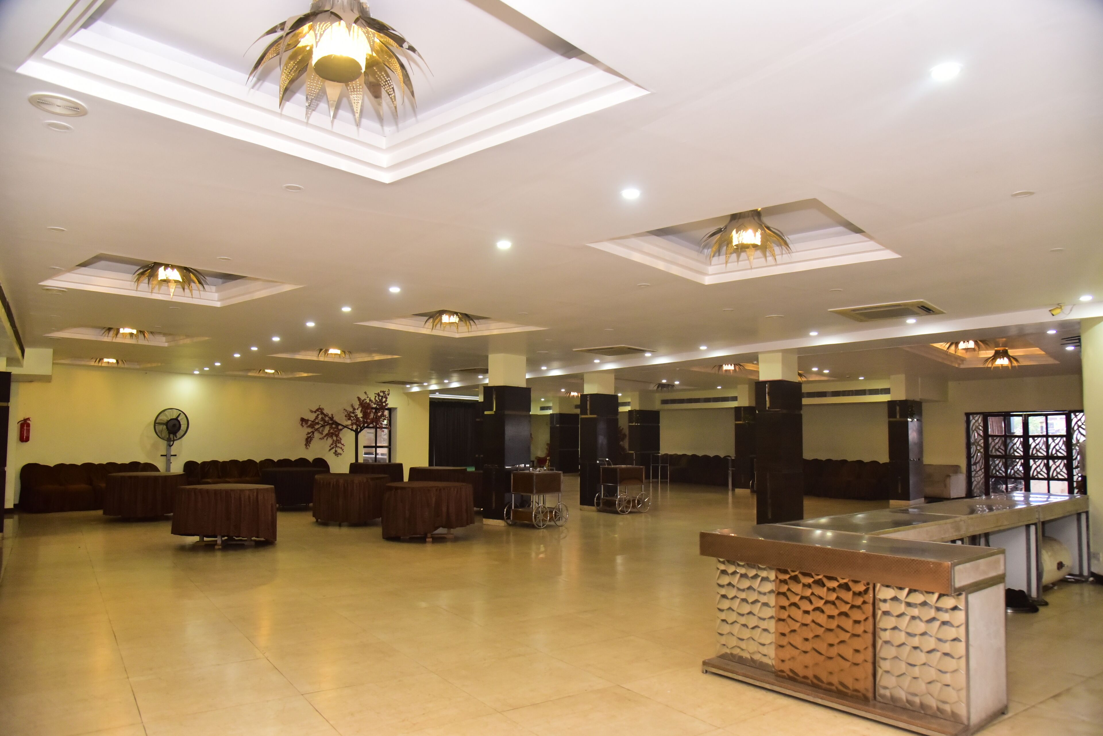 A spacious hotel lobby with multiple seating areas, a reception desk, and a large fan.