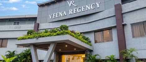 A building with a sign reading 'VENA REGENCY' and a covered entrance area with potted plants.