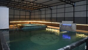 An indoor swimming pool with a tiled floor, a hot tub, and a waterfall feature. - VEENA REGENCY (Chas)