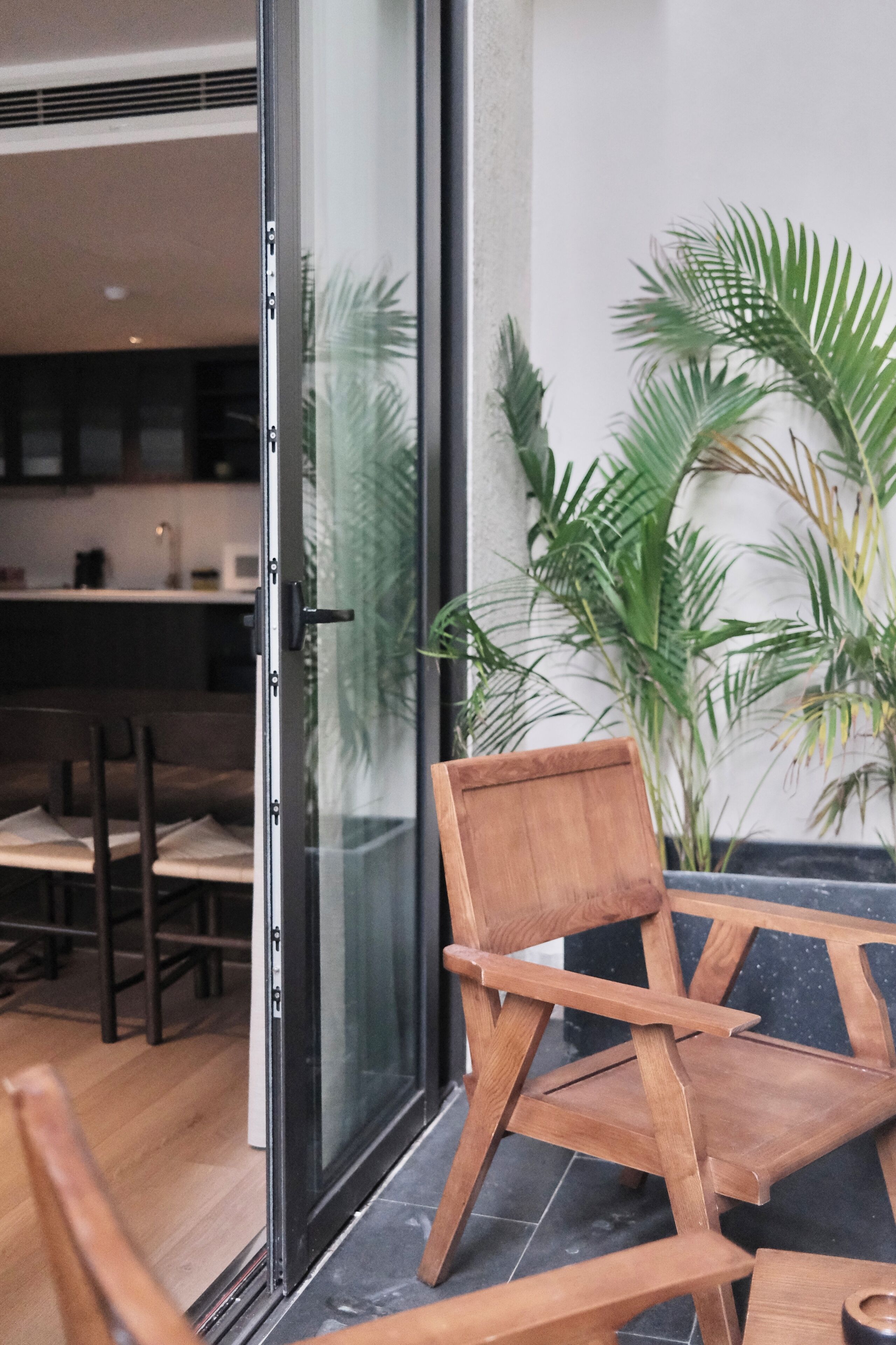 A wooden chair near a glass door, a dining area with chairs, and a potted plant.