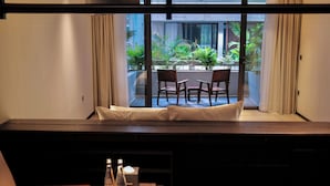 Une chambre d’hôtel avec vue sur un balcon, un coin salon avec une table et une fenêtre avec des rideaux.