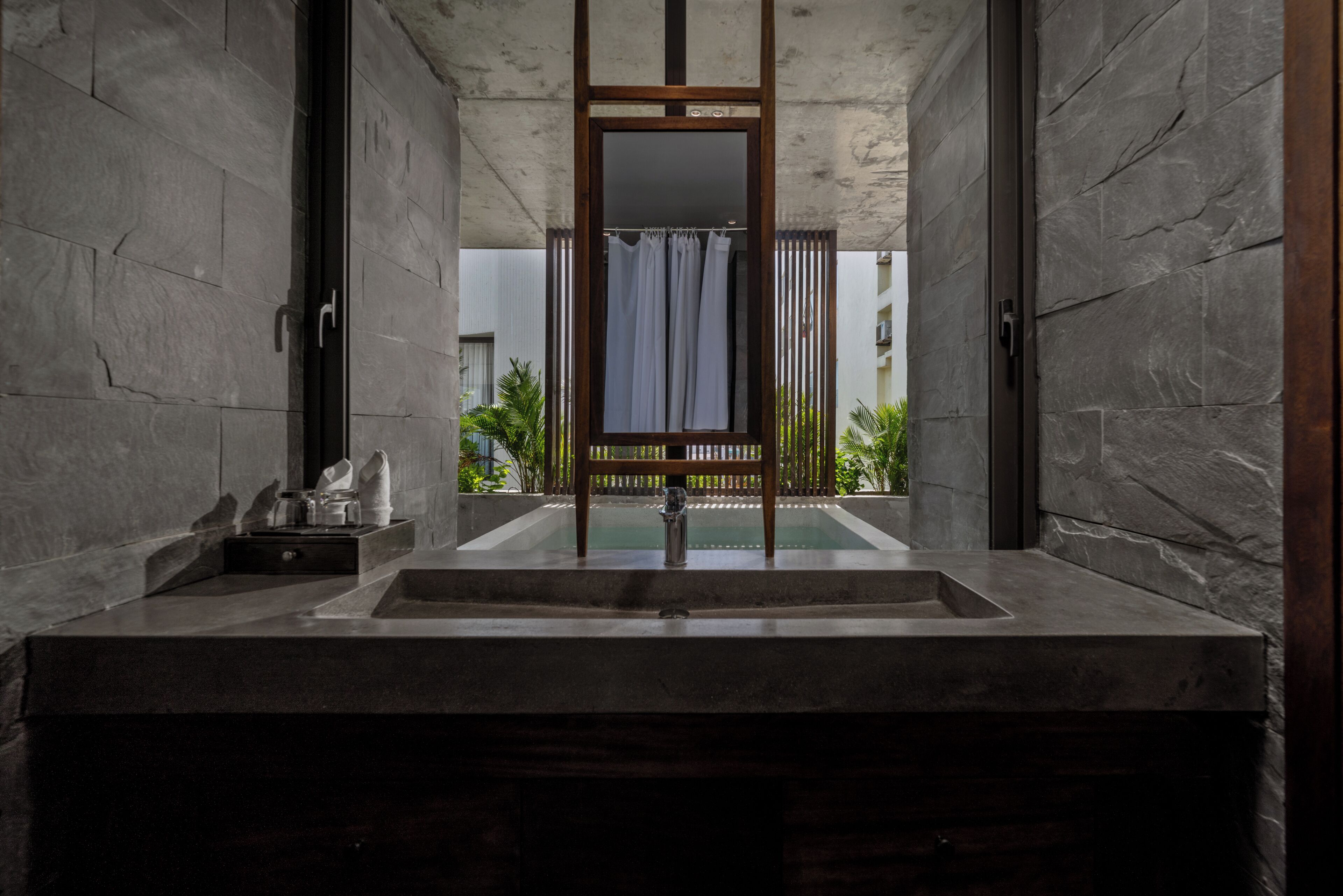 A modern bathroom with a large mirror, a sink, and a view of a pool and greenery.