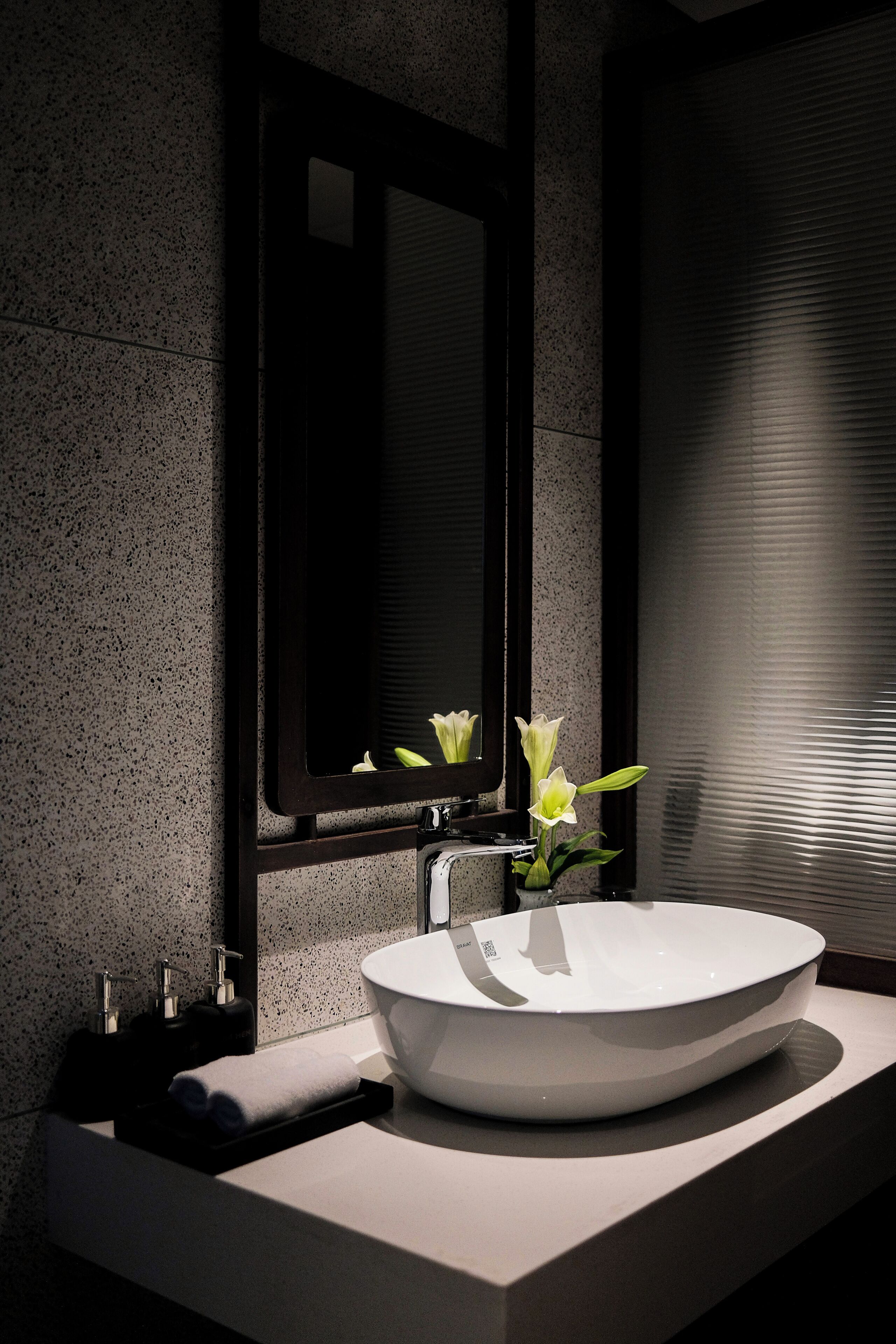 Een moderne badkamer met een grote witte wasbak, een spiegel en een vaas met bloemen.