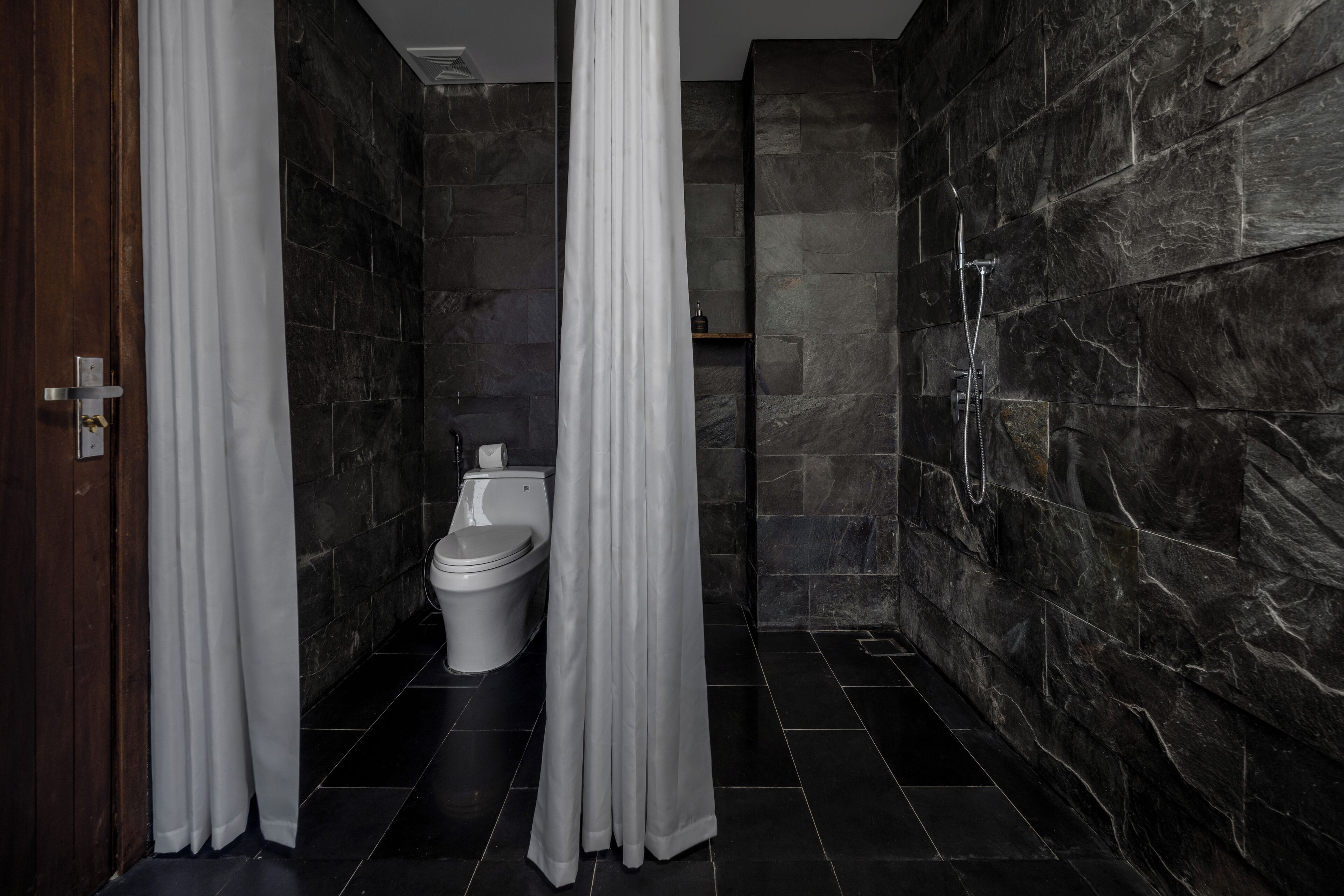Un baño moderno con inodoro, ducha y paredes de piedra oscura.