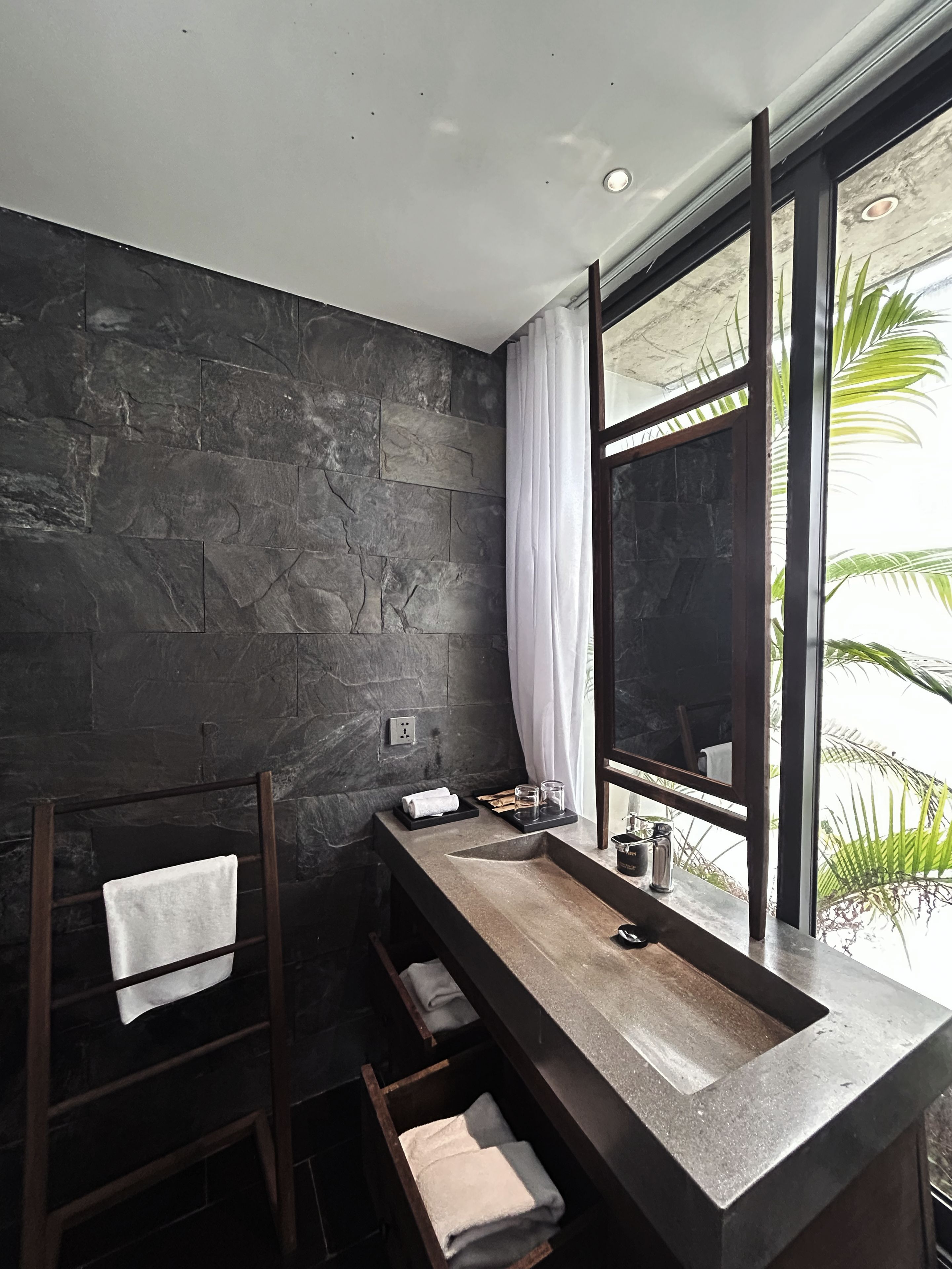 A modern bathroom with a stone wall, a wooden ladder, a large window, and a built-in sink.