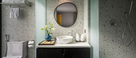 A modern bathroom with a freestanding toilet, a white sink with a round mirror, and a shower area.