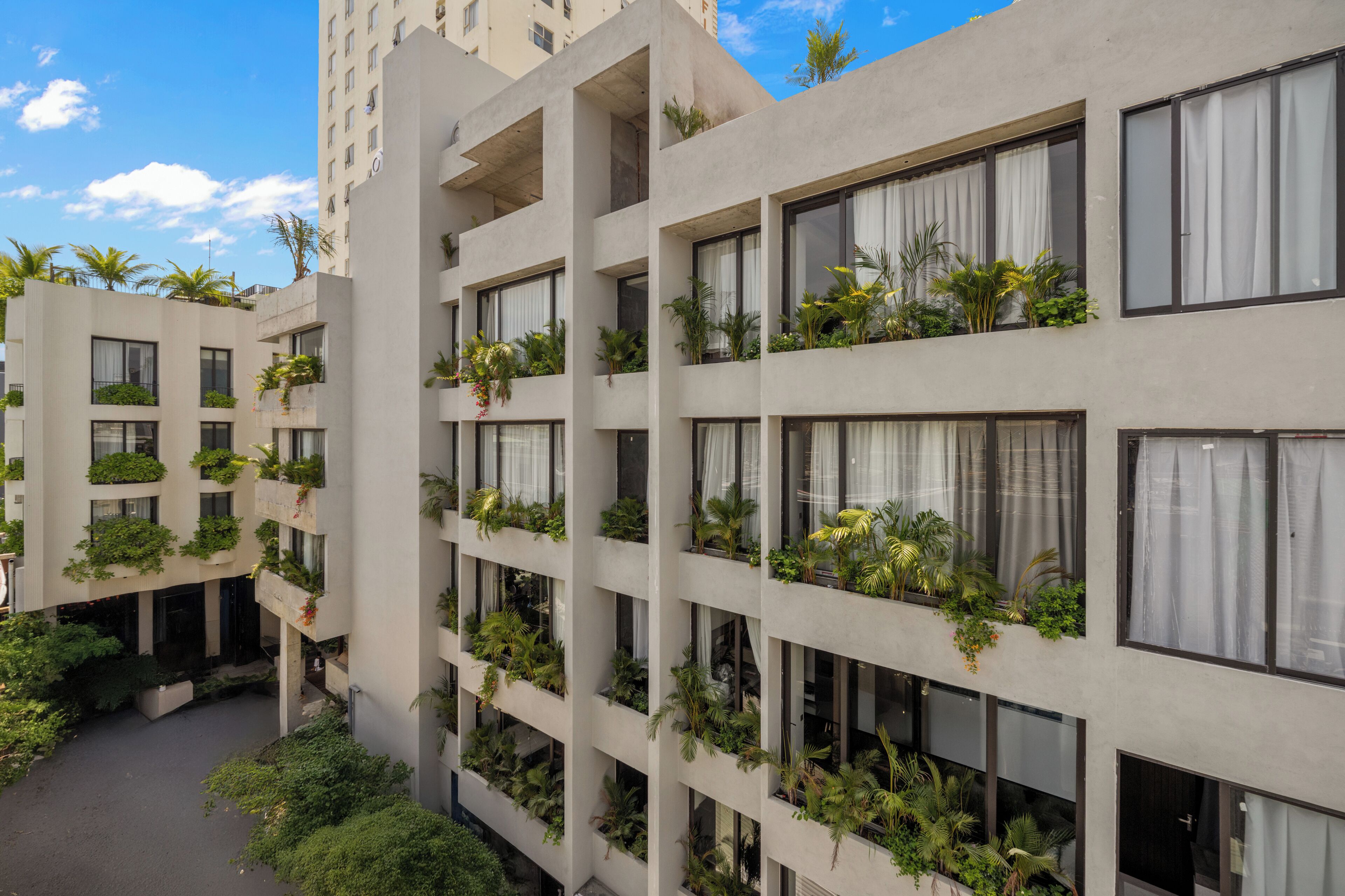 Un hôtel à plusieurs étages, doté de balcons ornés de plantes, d’une cour intérieure et surplombant un ciel d’un bleu éclatant.