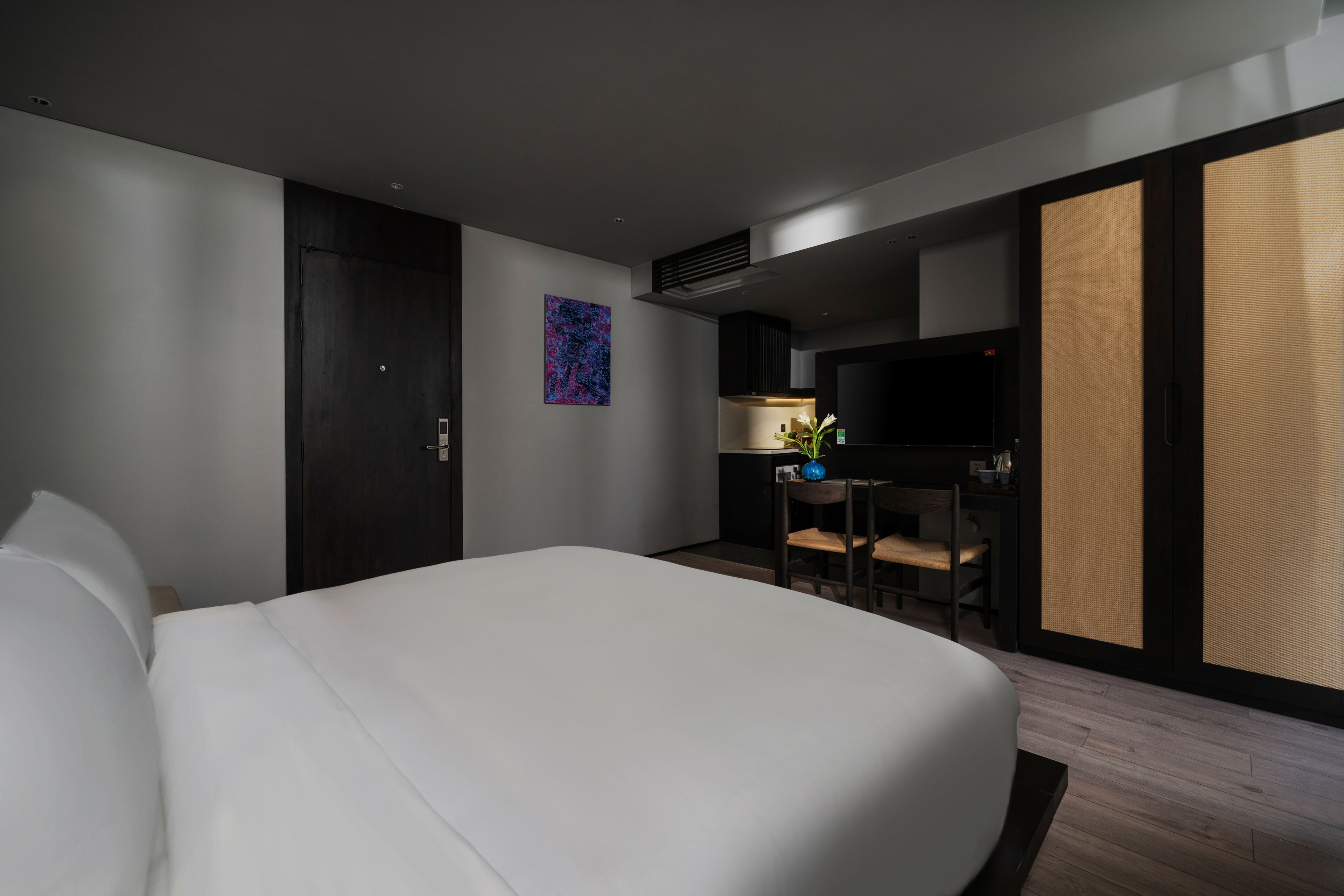 A modern hotel room with a large bed, a desk with a chair, a flat-screen TV, and a decorative plant.