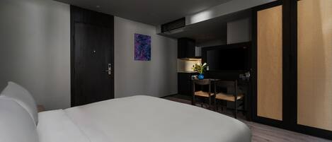 A modern hotel room with a large bed, a desk with a chair, a flat-screen TV, and a decorative plant.