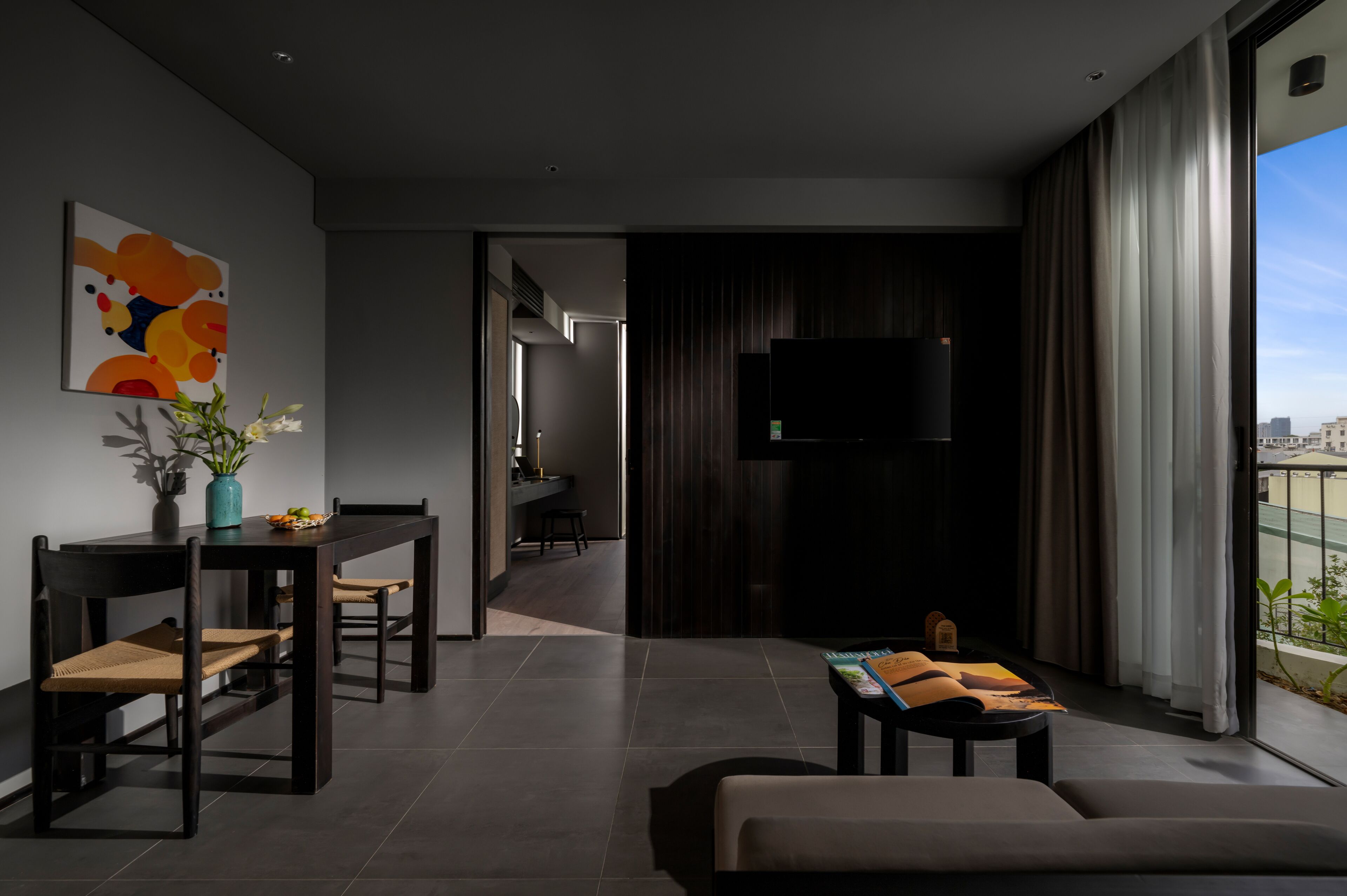 A modern living room with a dining area, a flat-screen TV, and a large window with a city view.