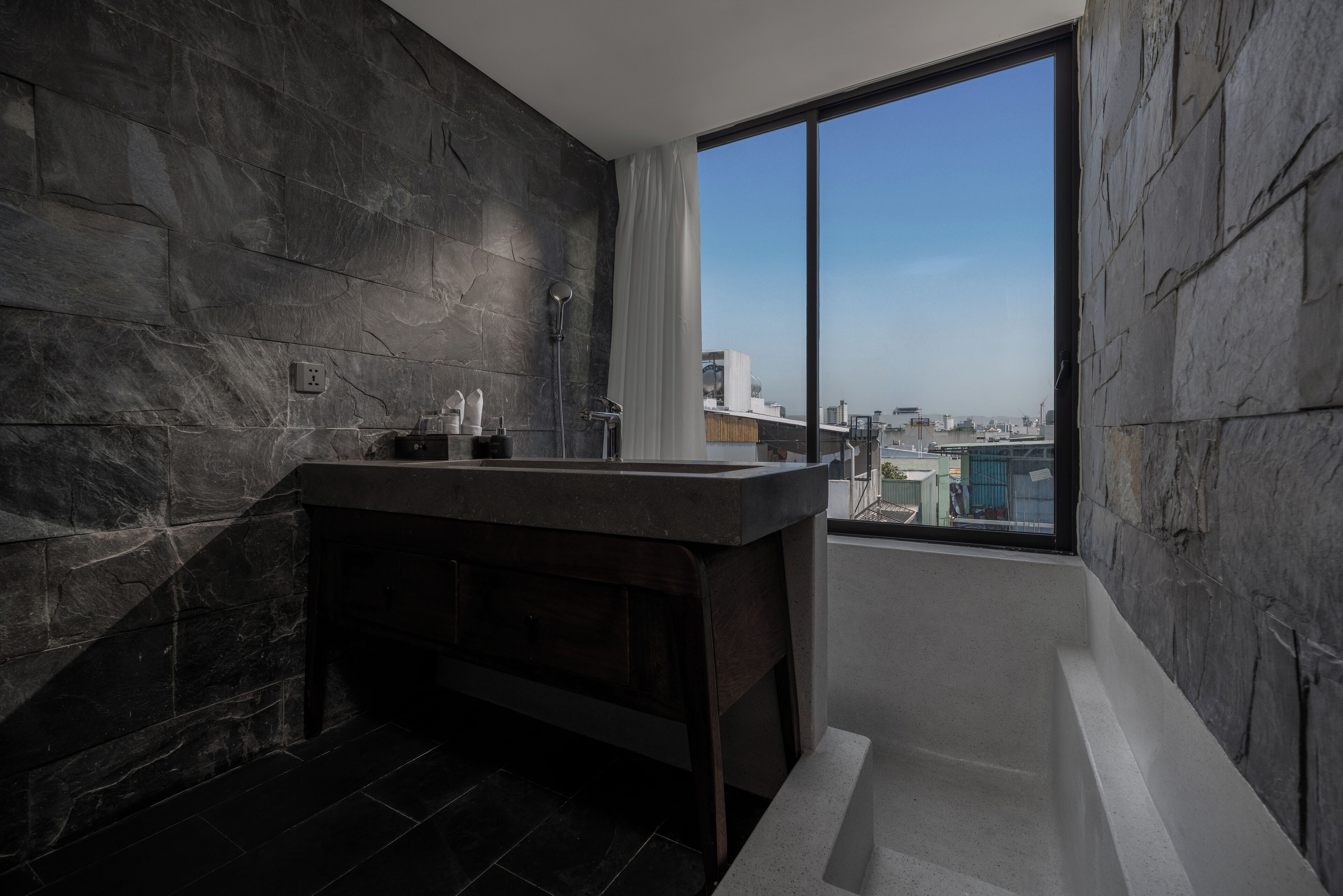 A modern bathroom with a large window, a bathtub, and a vanity with a mirror.
