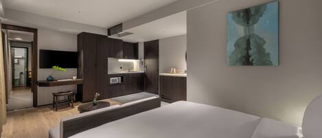 A modern hotel room with a large bed, a desk with a computer, a microwave, and a small seating area.