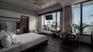 Une chambre d’hôtel moderne, dotée d’un grand lit, d’un bureau et d’une télévision. De grandes fenêtres, équipées de rideaux, offrent une vue sur la ville.