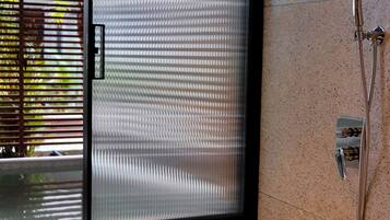 A bathroom with a frosted glass door, a showerhead, and a tiled floor.