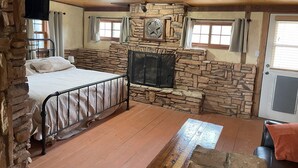 Une pièce chaleureuse avec une cheminée en pierre, un lit avec un cadre en métal et un plafond en bois.