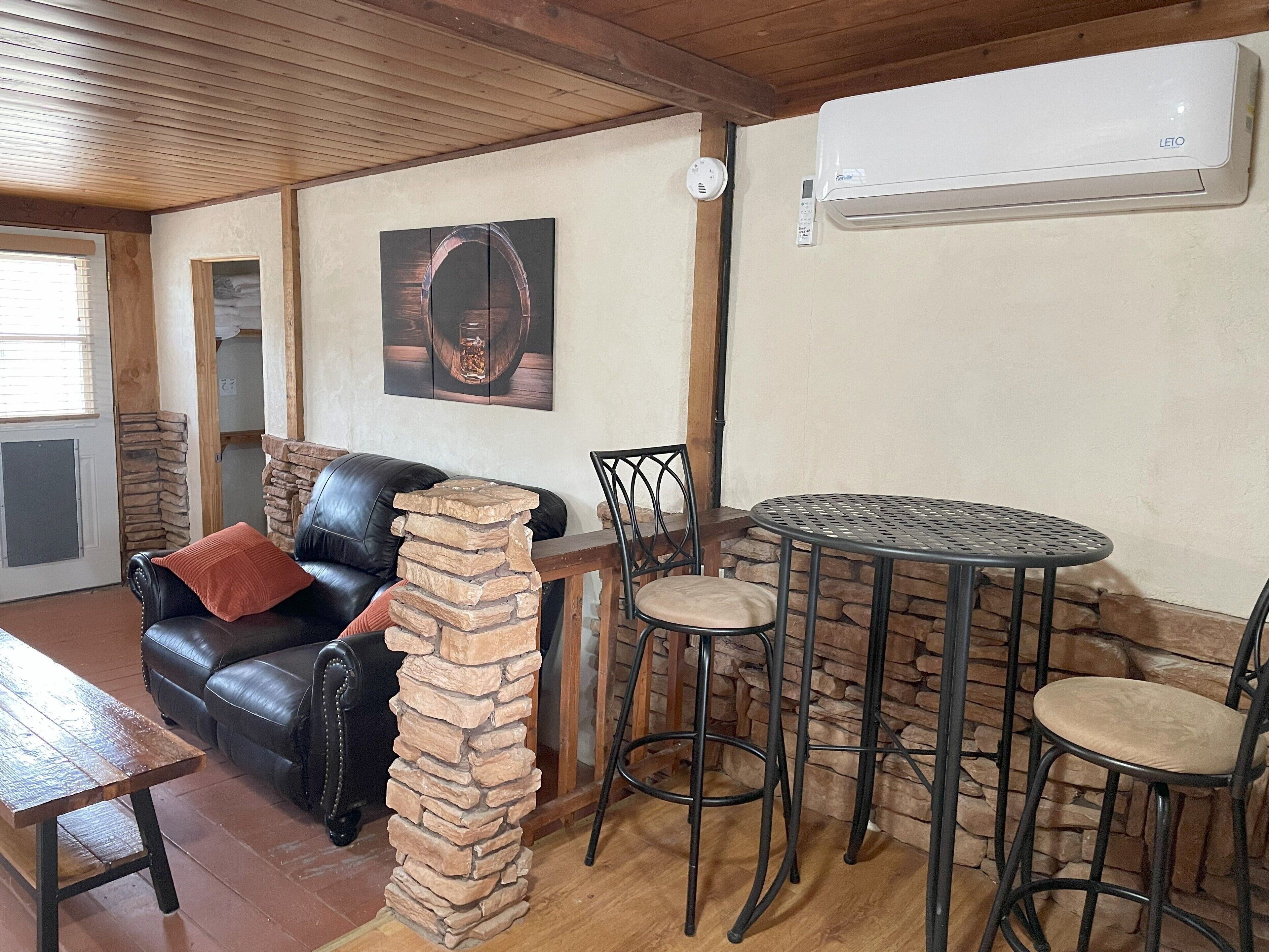 A cozy living area with a black leather sofa, a stone pillar, a round metal table, and two chairs.