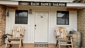 Un bâtiment rustique, sur lequel on peut lire l’inscription « The Rain Dance Saloon ». Devant une porte blanche portant le numéro 14, on aperçoit deux fauteuils à bascule.