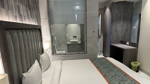 Een moderne hotelkamer met een groot bed, een badkamer met een glazen douchecabine en een klein zithoekje met een kamerbreed tapijt.