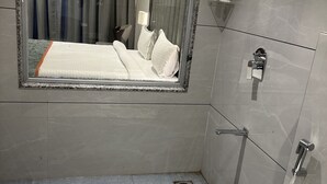 Een moderne badkamer met een grote spiegel, een douchegedeelte en een bed met witte lakens.
