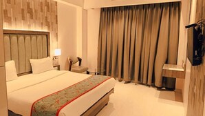 Hotelkamer met een bed, bureau, stoel, televisie en raam met gordijnen.