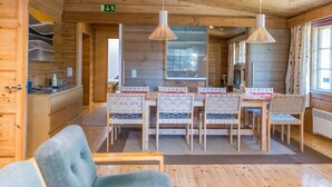 Un interior de madera con zona de comedor que incluye una mesa y sillas, un sofá y una cocina con estufa y armarios.
