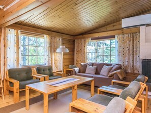 A cozy cabin interior with wooden walls and ceiling, a sofa, chairs, a table, and a fireplace.