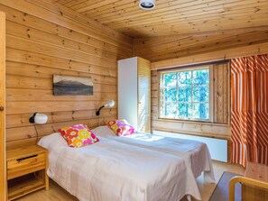 A cabin with two beds, a wooden headboard, a nightstand, a bedside lamp, a window with curtains, and a wall-mounted picture.