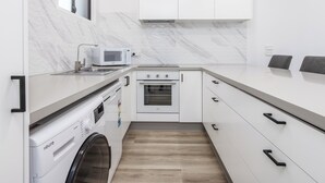 Eine moderne Küche mit weißen Schränken, einer eingebauten Mikrowelle, einer Waschmaschine und einem kleinen Backofen.