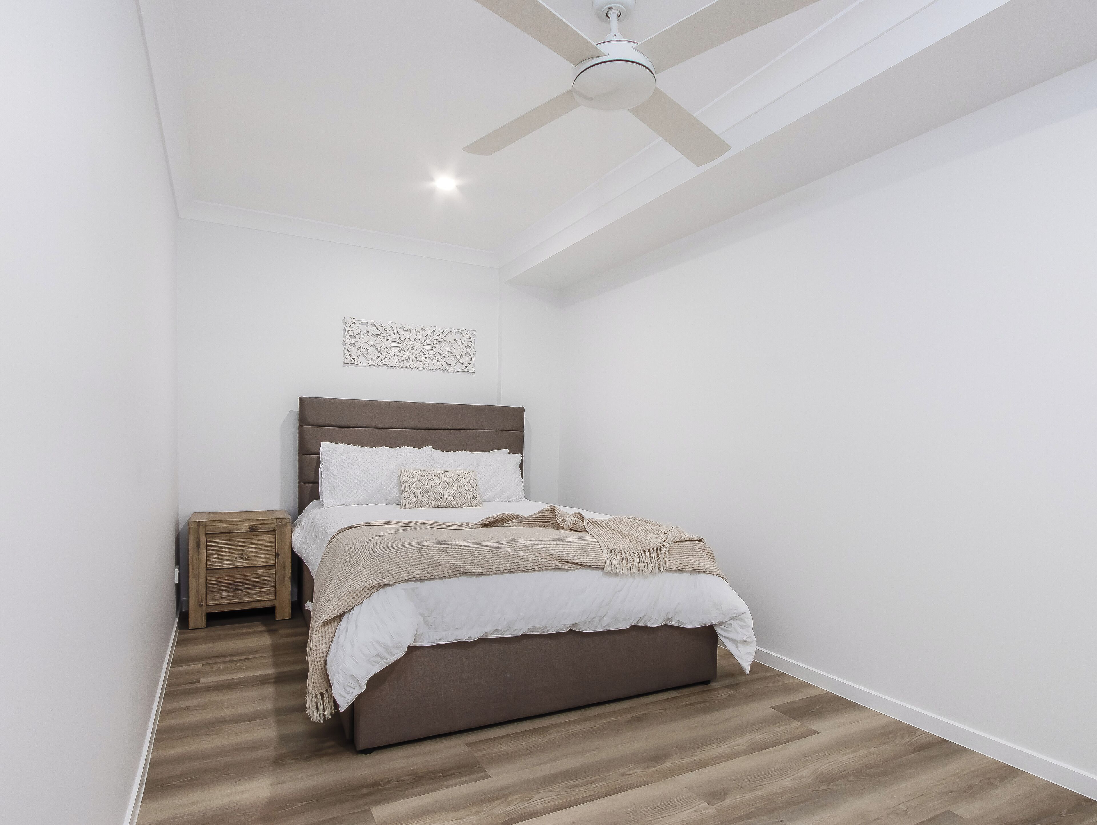 Una camera da letto con un letto, un comodino, una ventola a soffitto e un elemento decorativo a parete.