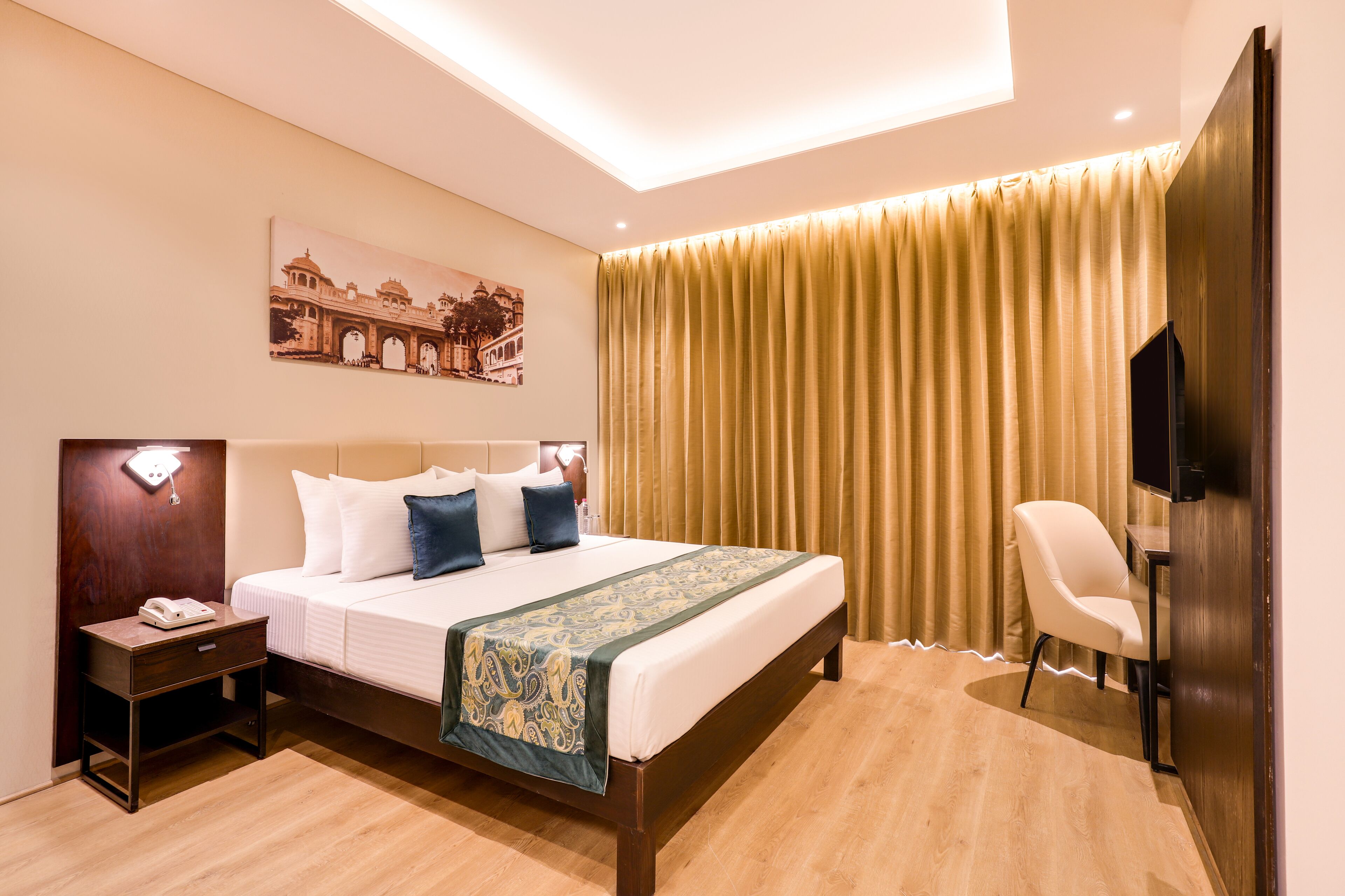 A hotel room with a bed, bedside table, chair, and a painting on the wall.