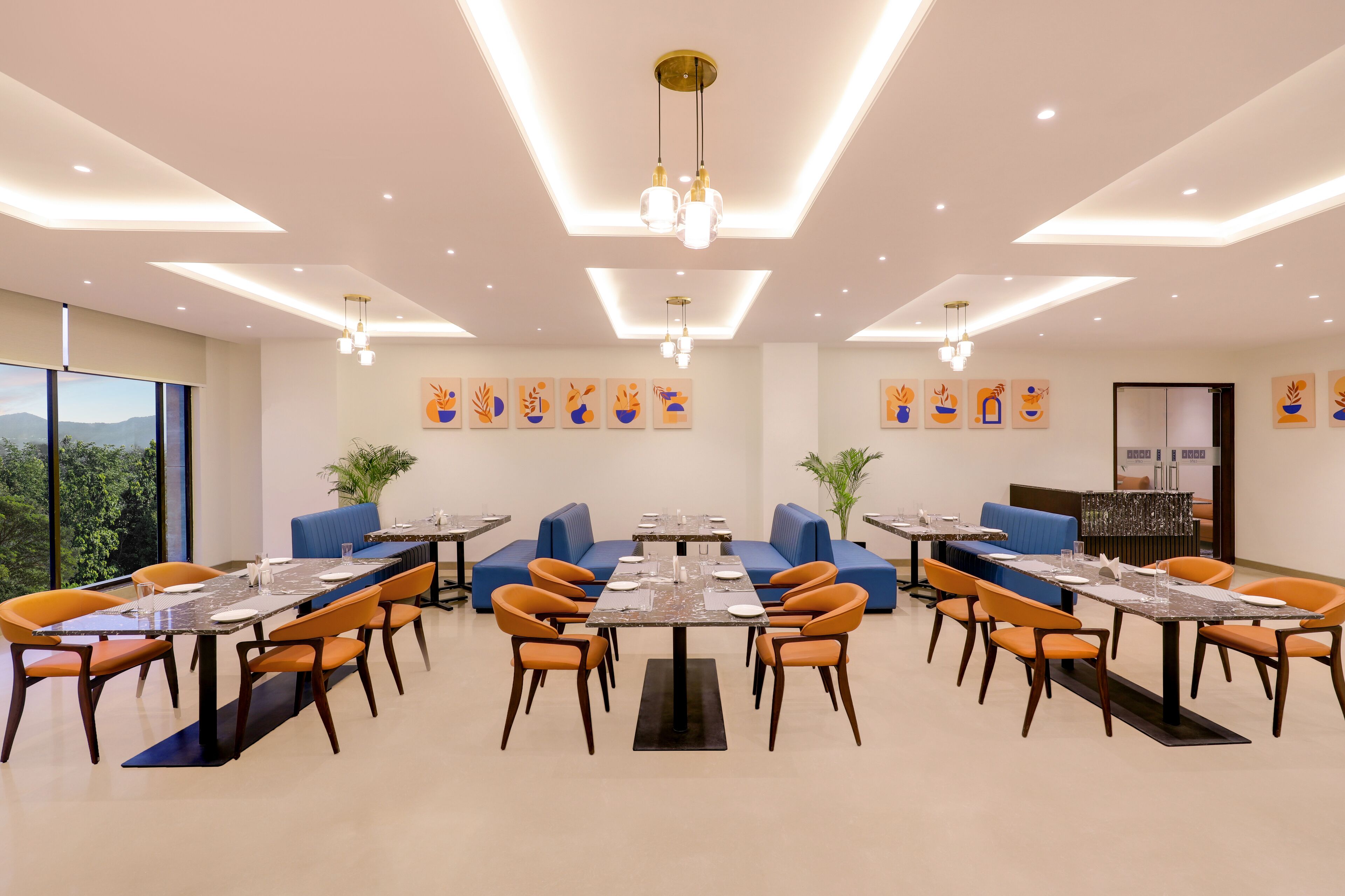 Un espace de restauration moderne, doté de plusieurs tables et chaises, d’un éclairage au plafond et d’œuvres d’art accrochées aux murs.