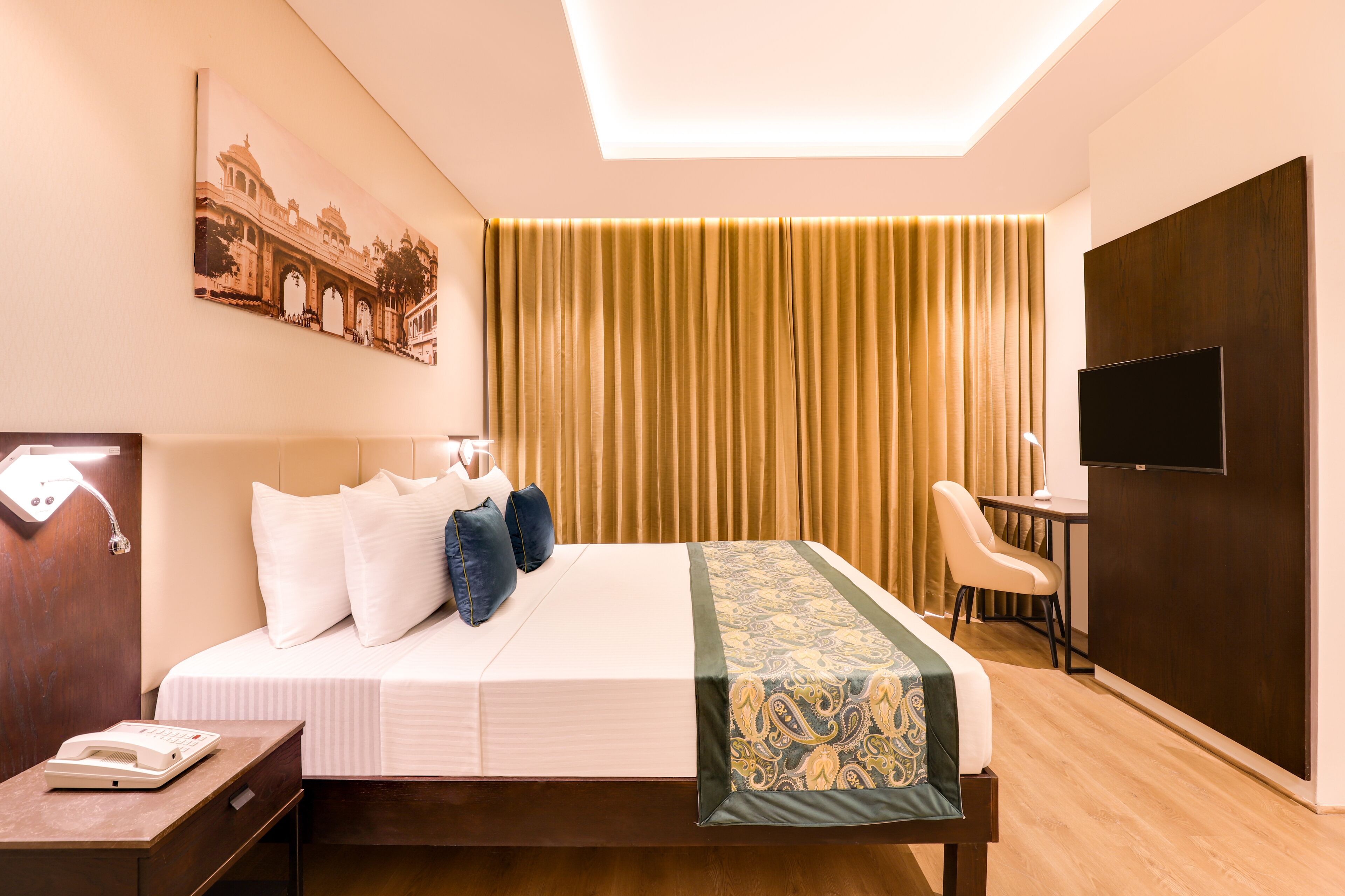 A hotel room with a bed, bedside table, desk, chair, TV, and curtains.