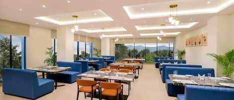 Un comedor moderno con asientos azules, mesas dispuestas con platos y vasos blancos, e iluminación empotrada en el techo.