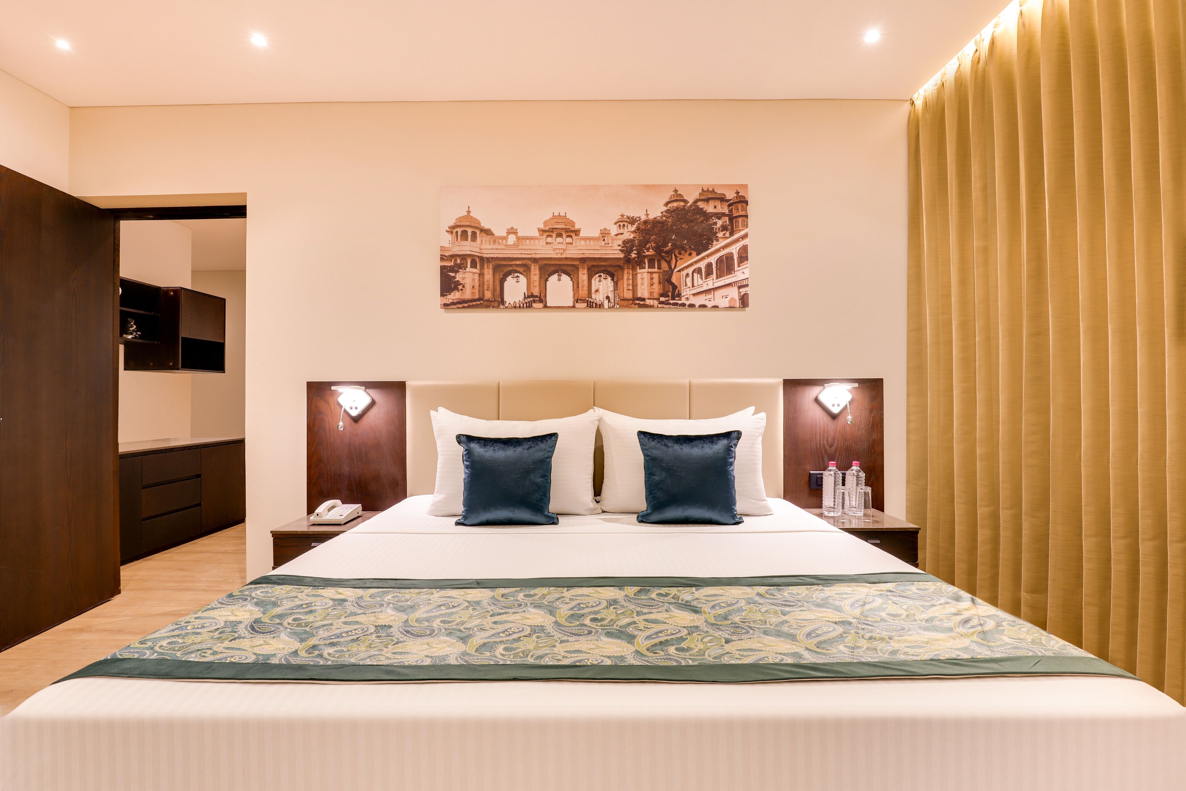 Une chambre d’hôtel avec un grand lit, deux tables de chevet, une petite table d’appoint, un téléphone fixé au mur et un élément décoratif mural.