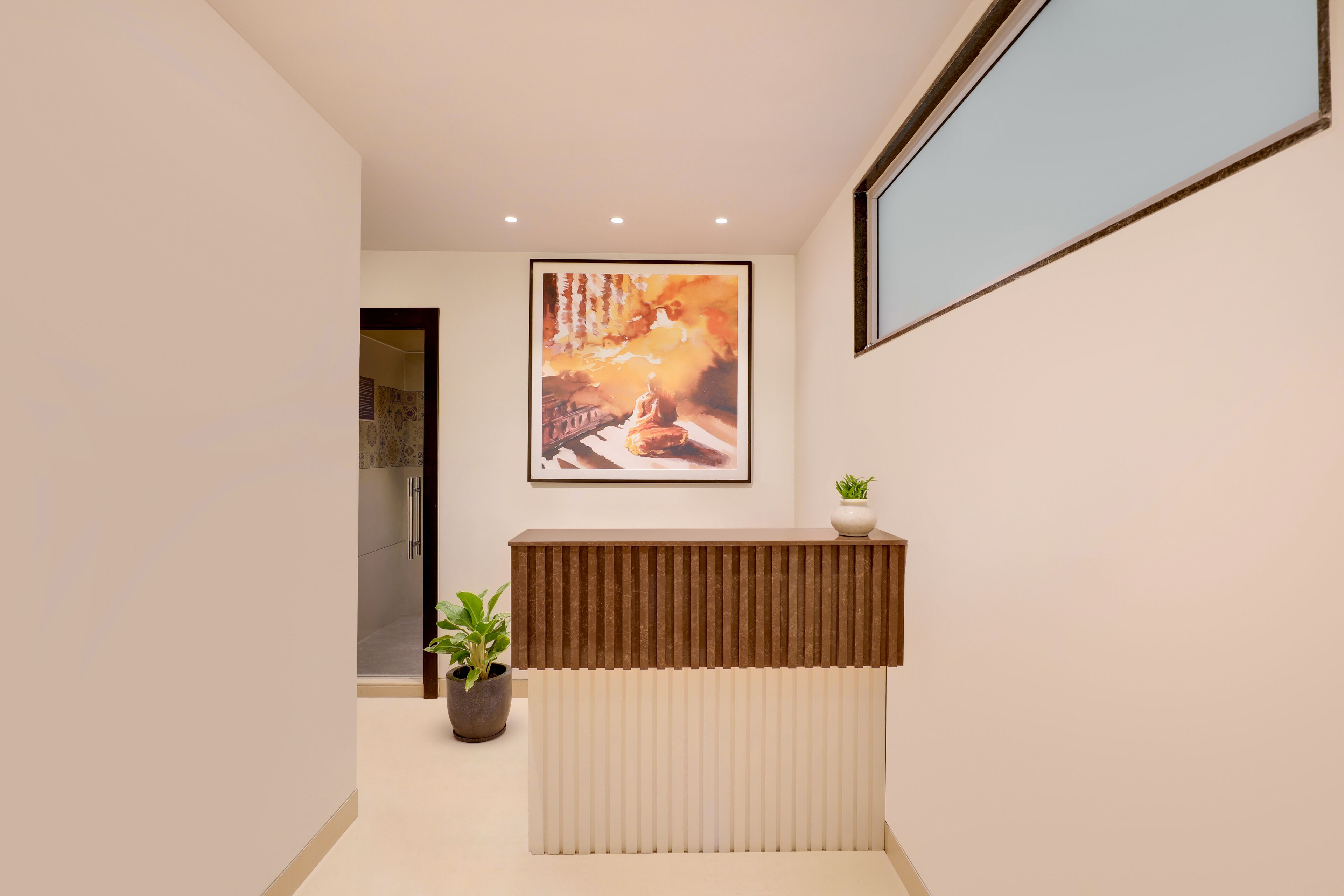A reception area with a modern design, featuring a reception desk, a framed artwork on the wall, and a potted plant.