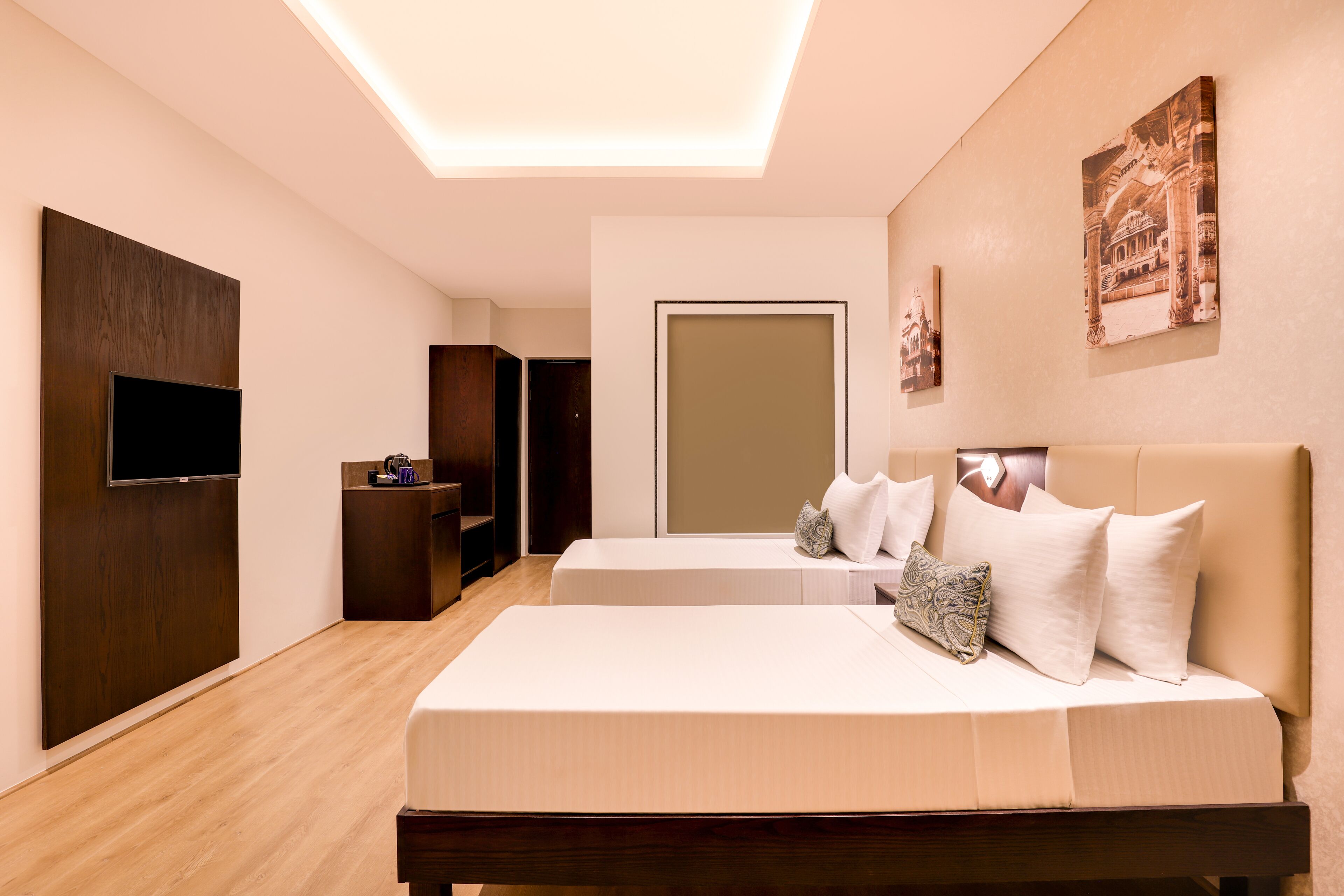 Een hotelkamer met twee bedden, een flatscreen televisie, een houten kast en een deur naar een andere kamer.