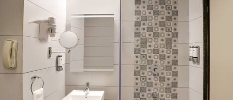 Un baño moderno con un lavamanos blanco, un espejo, un perchero para toallas, una ducha con azulejos estampados y un dispensador de papel higiénico.