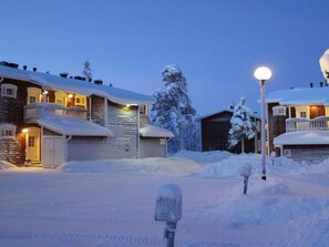 A snow-covered outdoor area with a building that has a stone facade and a wooden deck. - Rautulampi g15 by Interhome (Inari)