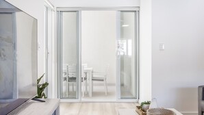 A modern living room with a flat-screen TV, a sliding glass door leading to a dining area, and a light-colored wooden floor. - 3 Bedroom Beachside Haven in Burleigh Heads (Gold Coast)