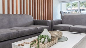 A modern living room with a grey sectional sofa, a white coffee table with decorative items, and a wooden slat wall. - 3 Bedroom Beachside Haven in Burleigh Heads (Gold Coast)
