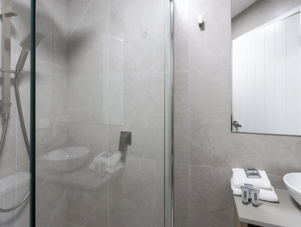 Un baño moderno con ducha de vidrio, lavamanos y espejo.