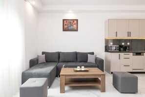 Un salon moderne avec un canapé d’angle gris, une table basse en bois et un pouf gris.