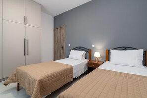 Une chambre d’hôtel avec deux lits simples, une armoire, une porte en bois et une table de chevet avec une lampe.