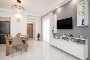 Uma cozinha moderna com forno embutido, mesa de jantar com cadeiras, uma planta em vaso e uma TV fixada na parede.