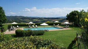 A poolside area with lounge chairs and umbrellas, surrounded by well-maintained lawns and hedges, with a view of rolling hills in the background. - Apartment in Montone with Pool & Garden (Montone - Umbertide (pg))