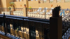A balcony with a decorative metal railing, potted plants, and a view of a building with beige walls and blue-tiled accents. - Ryad Marocain Proche D'agadir 15 Personnes - 6 Chambres - 3 sdb - 1 Piscine (Ifentar)