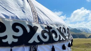 A white tent with black decorative patterns and tassels, set against a mountainous landscape. - Kel-Suu At-Bashy (Kel Suu)