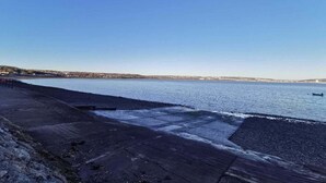 Ein Küstenweg mit freiem Blick auf das Meer und entfernte Gebäude.